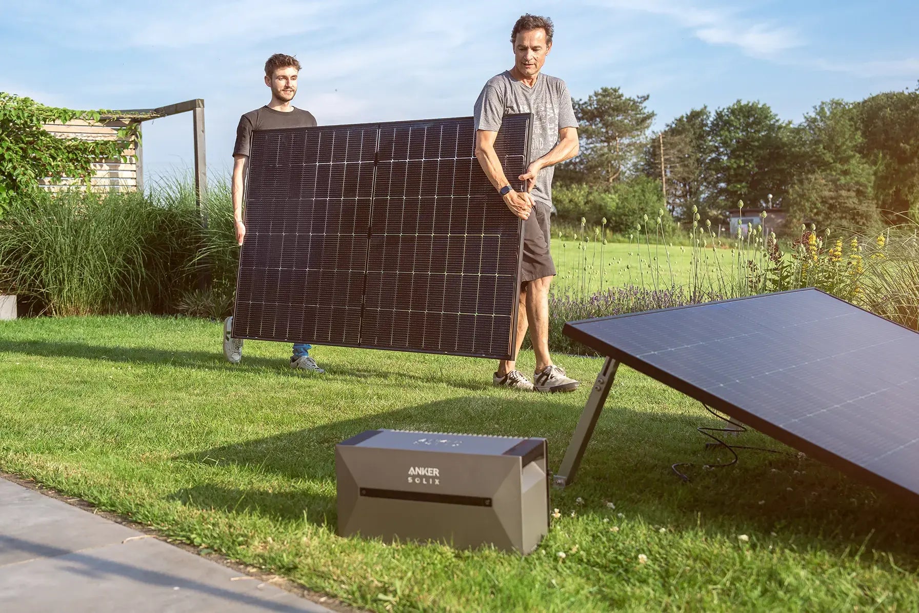 Zwei Männer installieren ein Balkonkraftwerk mit Speicher im Garten. Hier mit der Anker SOLIX Speicherlösung.