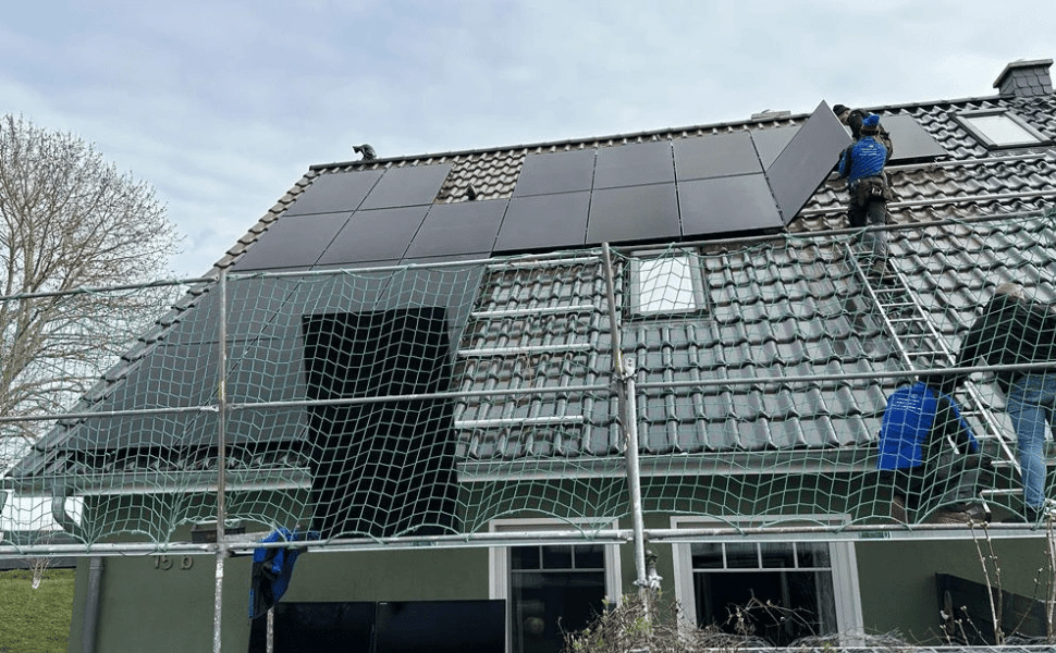 Arbeiter installieren Solarmodule auf dem Dach eines Hauses, das von einem Baugerüst umgeben ist