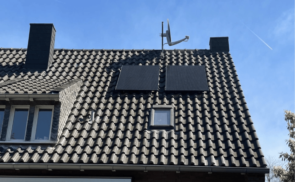 Solarmodule auf dem Dach eines Hauses mit Satellitenschüssel und klarem Himmel im Hintergrund